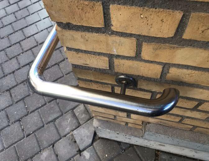 Löper förbi trappan sista steg och fortsätter som ett stöd. Andra sidan av trappan saknar ledstång.