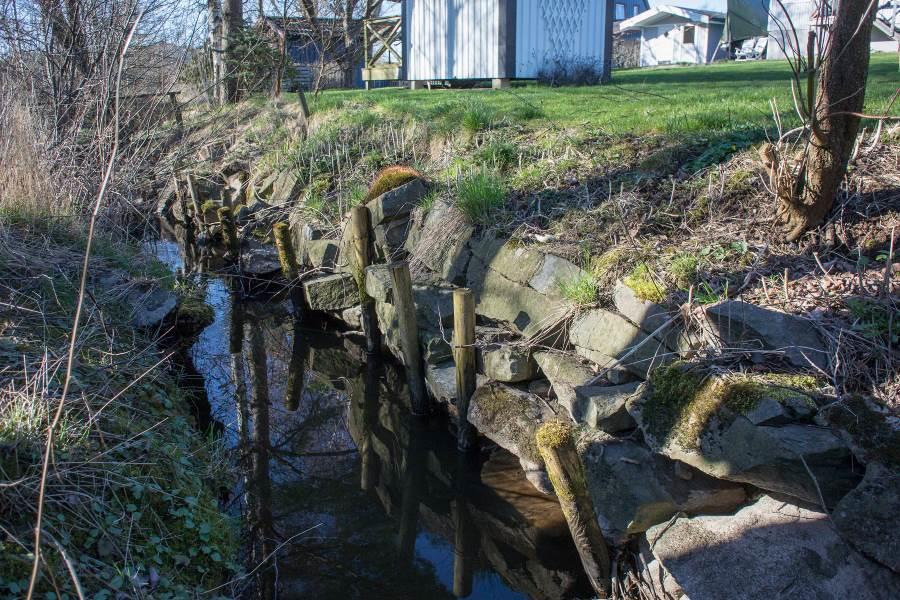 Där bäcken löper utmed tomt har den grävt sig in under gräsmatta om inte erosionsskydd finns i form av stenlagda kanter eller betongväggar.