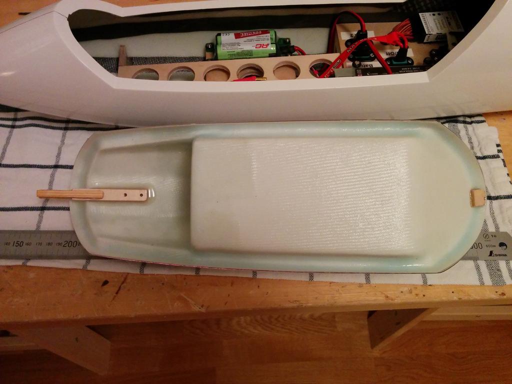 Här kan man se träbitarna som håller huven på plats. 11. Fastsättning av vingen. Vingen hålls på plats med två krokar plus en (ganska kraftig) fjäder.