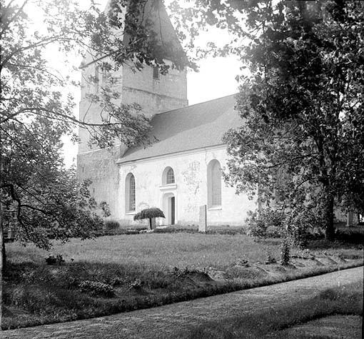 Till vänster om kyrkan syns den övergivna gamla kyrkogården, likaledes innanför en uppväxt trädkrans.