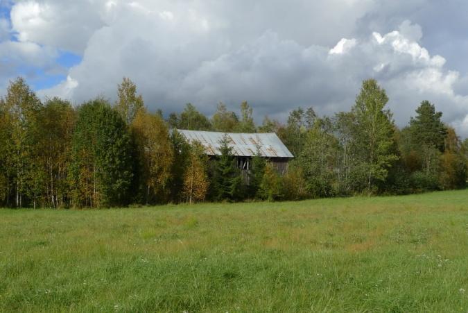 Objekt 34 Brädlada i sluttning intill en asfaltsväg. Ladan har tak av pannplåt och lutar ganska mycket.