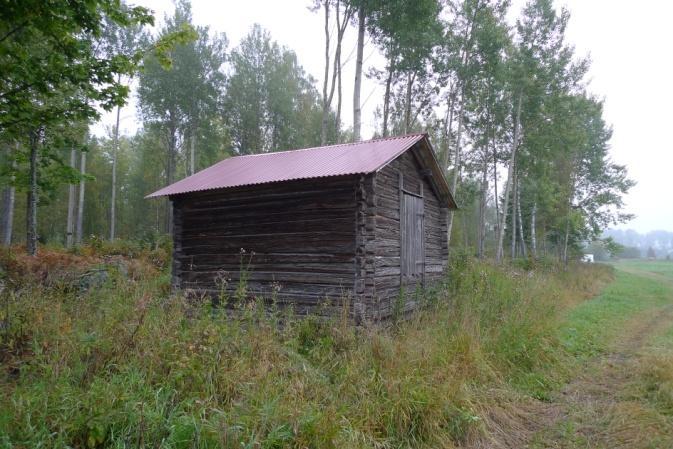 Söderala Objekt 54 Timmerlada med bilade stockar och plåttak som står i skogskanten intill en sädesåker (foto nedan t.v.).