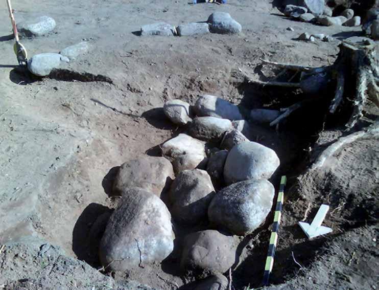Figur 19. Den rektangulära stenpackningen till skelettgrav A1475 framkom i sin helhet ca 0,3 m under marknivån. I bakgrunden syns delar av kantkedjan till graven. Foto från nordväst av Emma Sjöling.