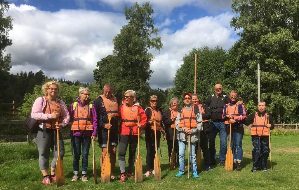Bildbeskrivning: 11 personer står på en gräsmatta utanför Kyrkekvarn med orange flytvästar på sig och med paddlar i händerna, redo för en tur på ån Tidan.