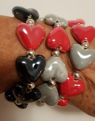 Armbanden består av handgjorda porslinshjärtan och nickelsäkra metallpärlor knutna på silikontråd. Smycket levereras i en organzapåse.