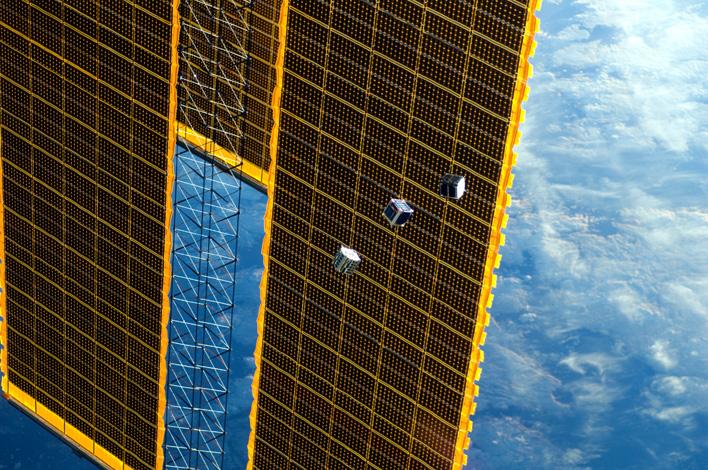 TechEdSat längst ned till vänster av de 3 satelliterna framför ISS solpanel med fördelningen att NASA hanterar prov och tester och att den svenska Rymdstyrelsen levererar tekniken genom ÅAC Microtec.