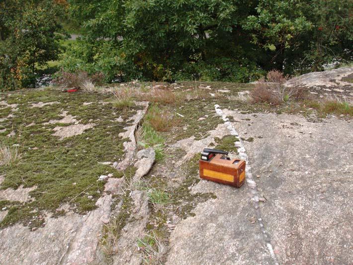 UG08087 7 (10) Foto 6: Berggrunden med kvartsfyllda sprickor som går vinkelrätt mot släntkanten, samt scintillometer för mätning av gammastrålning.