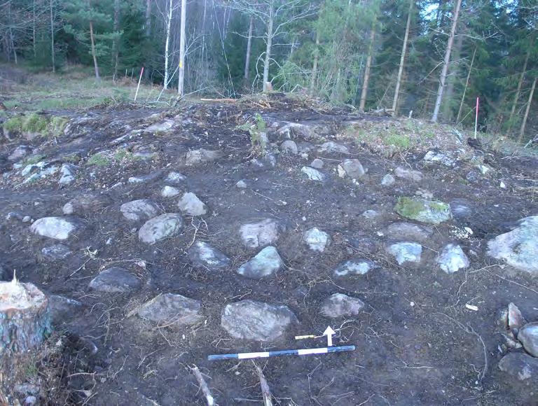 Bilaga 1. Anläggningsbeskrivningar A103 Stensättning, rund, 4,8 4,6 m stor och 0,25 m hög. Skadad. Rund stensättning med kantkedja och innanförliggande stenpackning (figur 13).