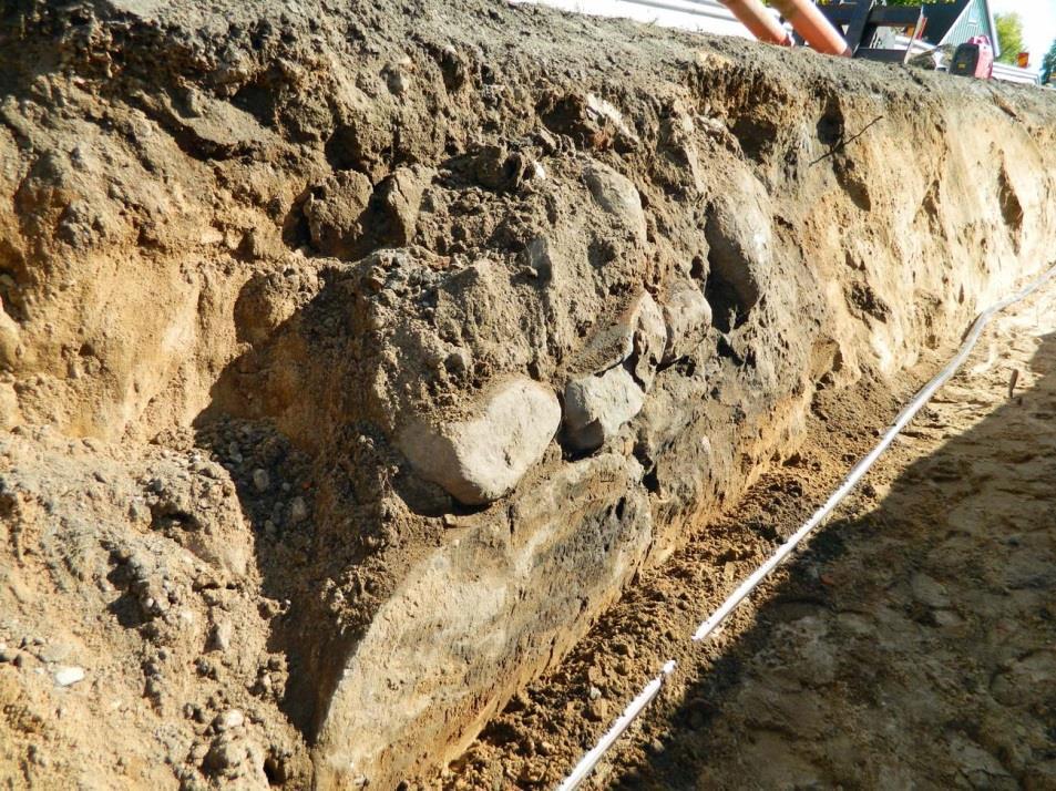Fig. 6. Kallmurad stenmur med kluvna, större stenar i nederdelen (litt. D). Den del av anläggningen som kunde påvisas löpte utmed schaktets östra sida. Foto mot sydöst, 29 september 2013. Fig. 7.