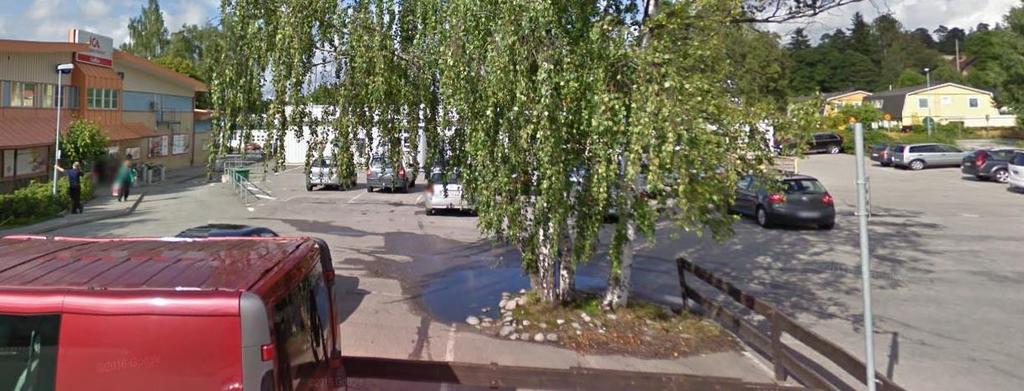 Figur 6 Planområdet sett från sydväst 1. T.v. om vita byggnaden (bakom träden) går en kant ner mot ett lågstråk där vatten avleds. Vid träden på parkeringen finns en lokal lågpunkt. 3.2.