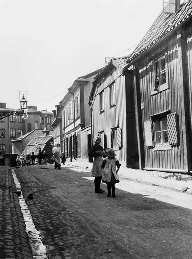 Folklivet på Breda gatan omkring sekelskiftet 1900. Breda gatan 4 syns bakom de två flickorna. SSMF003355S. Krigsmanskassan 8 är ett bostadshus i två våningar från 1969.